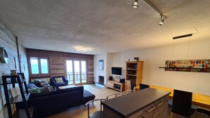 A modern living room with a sofa, a dining table, and a kitchen area. - Mountain Apartment With Parking (Veysonnaz)