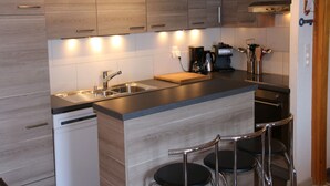 A modern kitchen with wooden cabinets, a stainless steel sink, a coffee maker, and two bar stools. - Mountain Apartment With Parking (Veysonnaz)