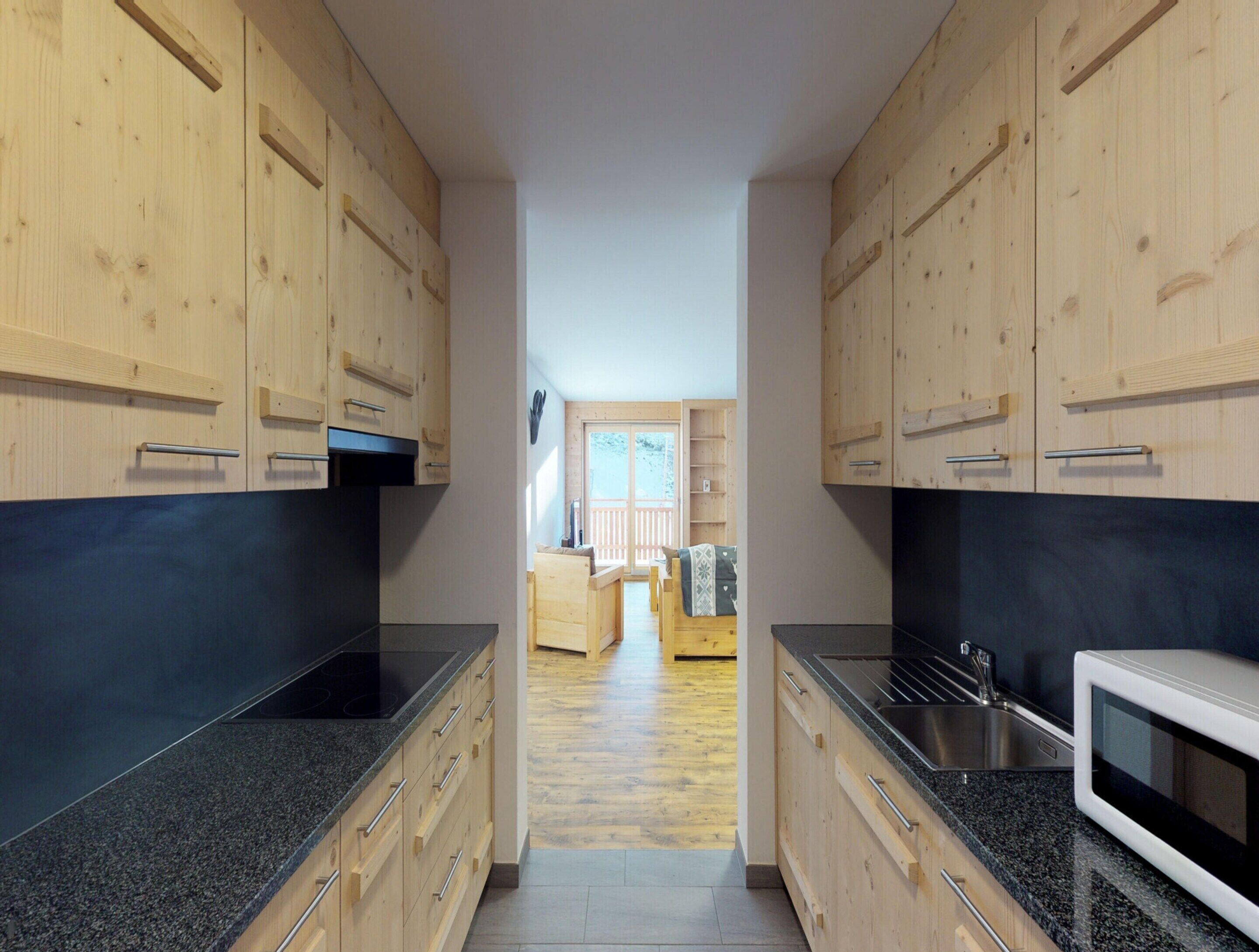 Una cocina estrecha con armarios de madera y encimeras de granito, que da paso a un comedor con una mesa y sillas de madera.
