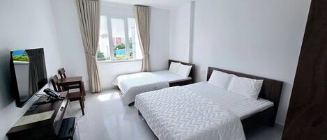 Ein Hotelzimmer mit zwei Betten, einem Schreibtisch, einem Stuhl, einem Fernseher und großen Fenstern mit Vorhängen.