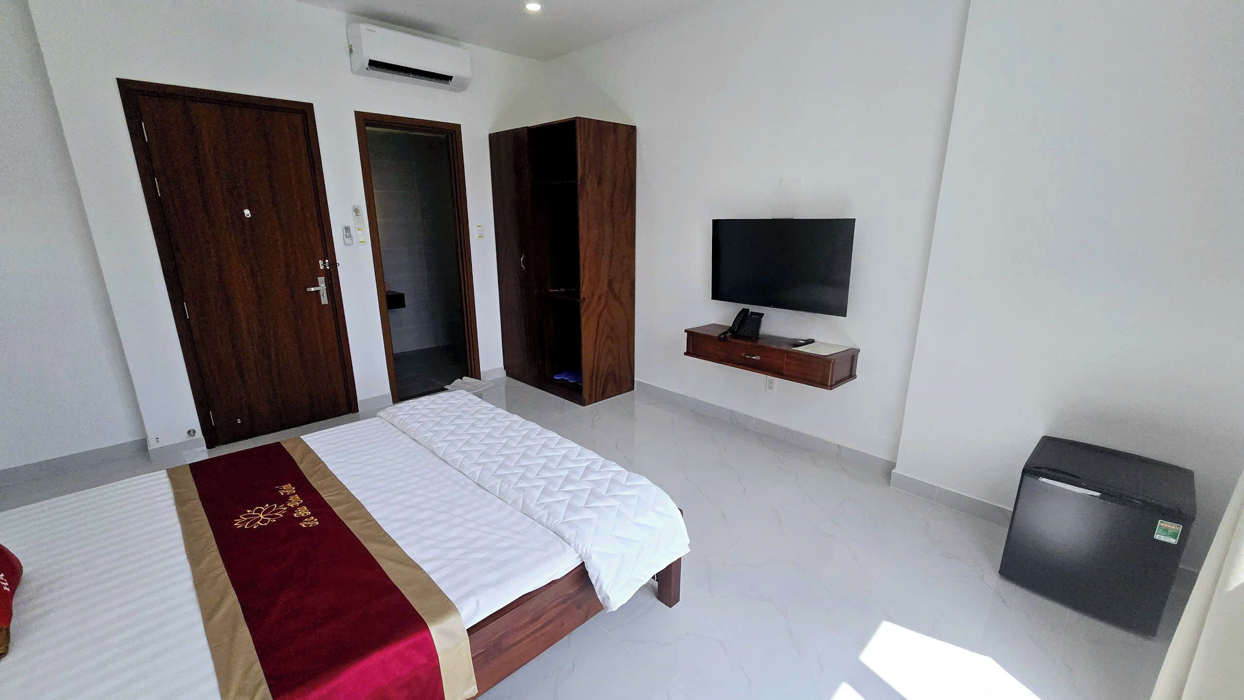 A hotel room with a bed, wardrobe, TV, and a small fridge.