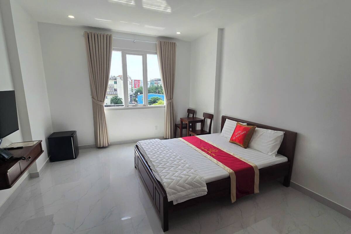 A hotel room with a bed, a TV, a desk with a phone, and a window with curtains.