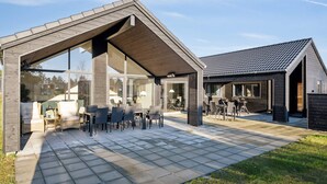Une maison moderne dotée d’un patio couvert aménagé avec du mobilier d’extérieur et d’une grande porte vitrée donnant sur l’intérieur.