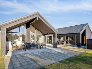 Uma casa moderna com um alpendre coberto, móveis de exterior e uma grande porta de vidro que dá para o interior.