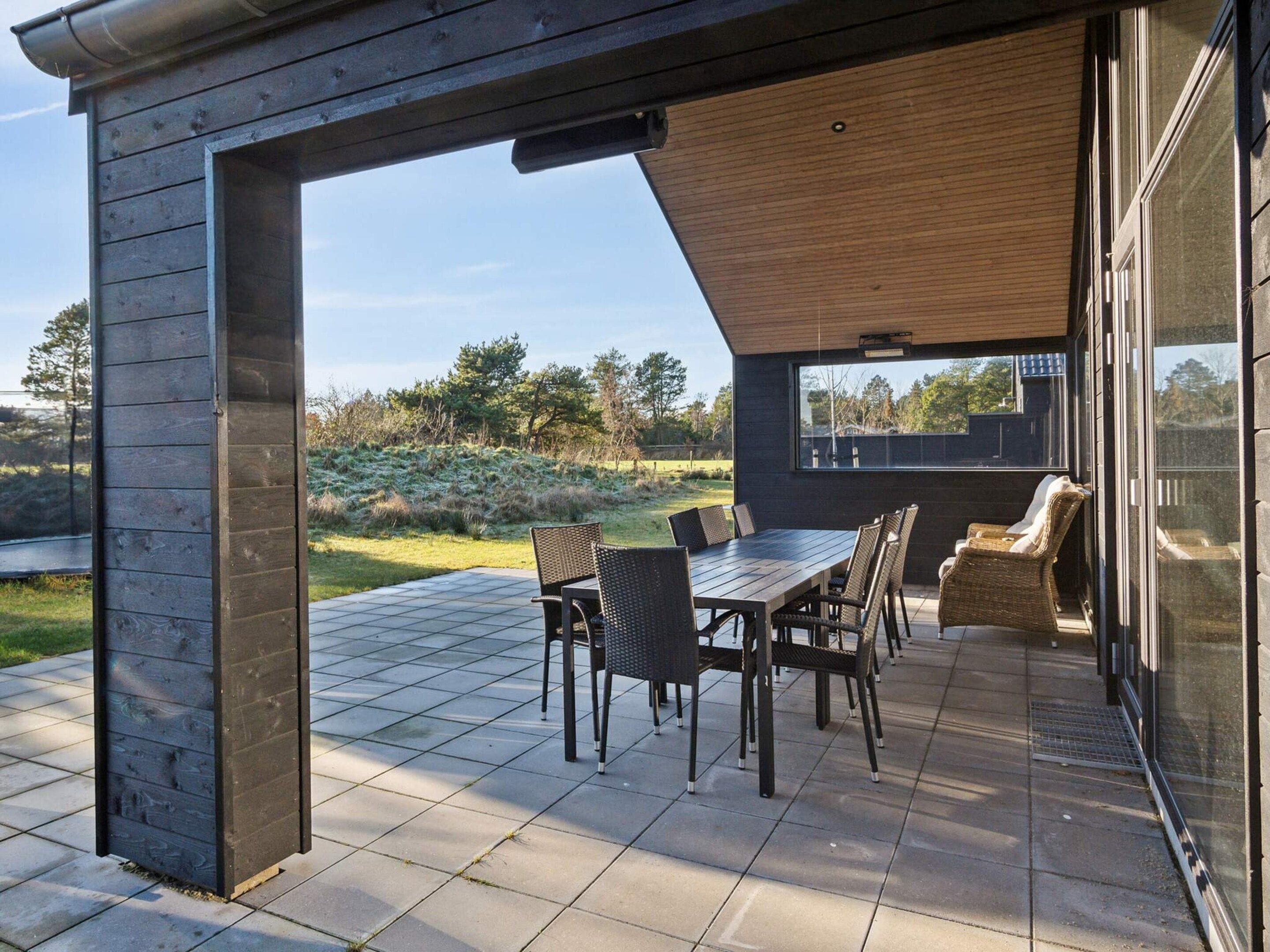 An outdoor patio with a table and chairs, a wooden pergola, and a view of the surrounding landscape.