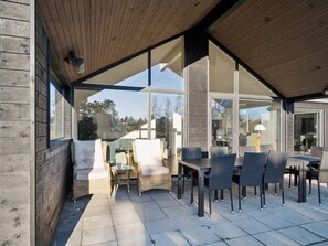 An outdoor patio with wicker furniture and a table, large glass windows, and a wooden ceiling.