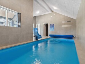 An indoor swimming pool with a blue slide, a bench, and a ceiling with recessed lighting.