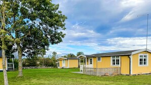 A row of yellow cabins with a grassy lawn and a tree in the foreground. - 4 Person Holiday Home in Lottorp (Löttorp)