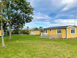 A row of yellow cabins with a grassy lawn and a tree in the foreground.
