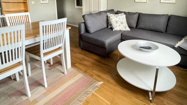 A living room with a grey sectional sofa, white chairs, a round coffee table, and a striped rug. - 4 Person Holiday Home in Lottorp (Löttorp)