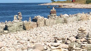 A rocky shoreline with stacked stones and a red building in the distance. - 4 Person Holiday Home in Lottorp (Löttorp)