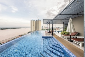 A rooftop infinity pool with lounge chairs and umbrellas, overlooking a cityscape and a body of water. - MekongView 6 Residence Sky Pool (Phnom Penh)