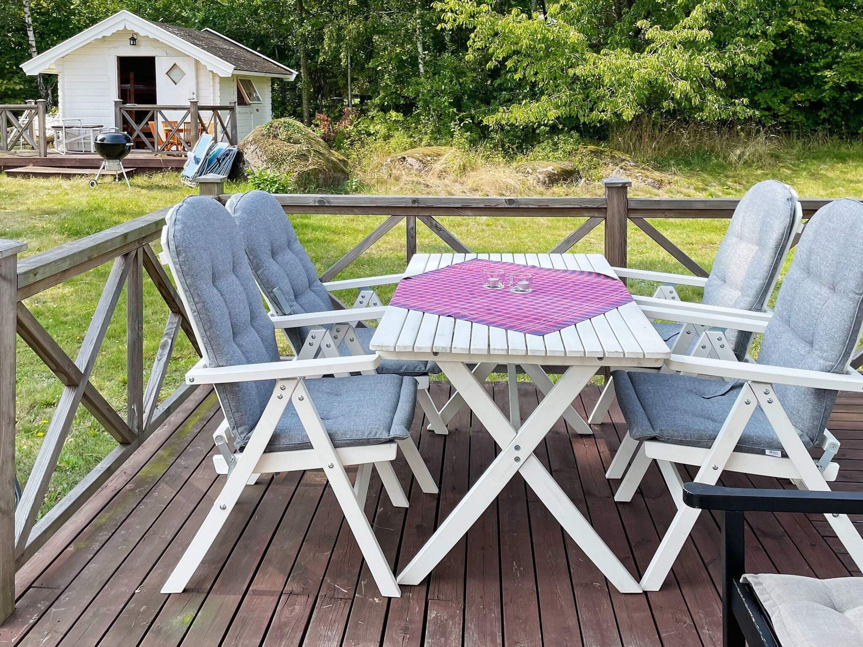 A deck with a table and chairs, a grill, and a small cabin in the background.