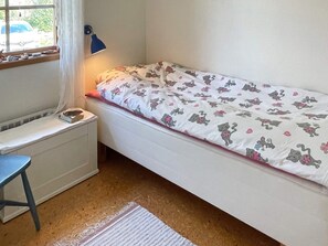 Una habitación pequeña con cama individual, ventana, escritorio y lámpara.