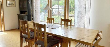 A dining area with a wooden table and chairs, a hanging light fixture, and a view through the windows.