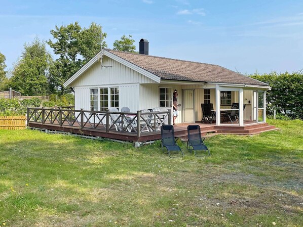 Ein eingeschossiges Haus mit überdachter Terrasse, einer Holzterrasse und einer kleinen Außen-Sitzgelegenheit.
