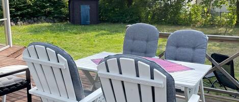 Una terraza al aire libre con mesa y sillas, un cobertizo pequeño y un patio cubierto de césped.