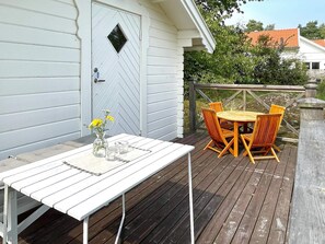 A wooden deck with a white table and orange chairs, a white door with a diamond-shaped window, and a wooden railing. - 8 Person Holiday Home in Borgholm (Borgholm)