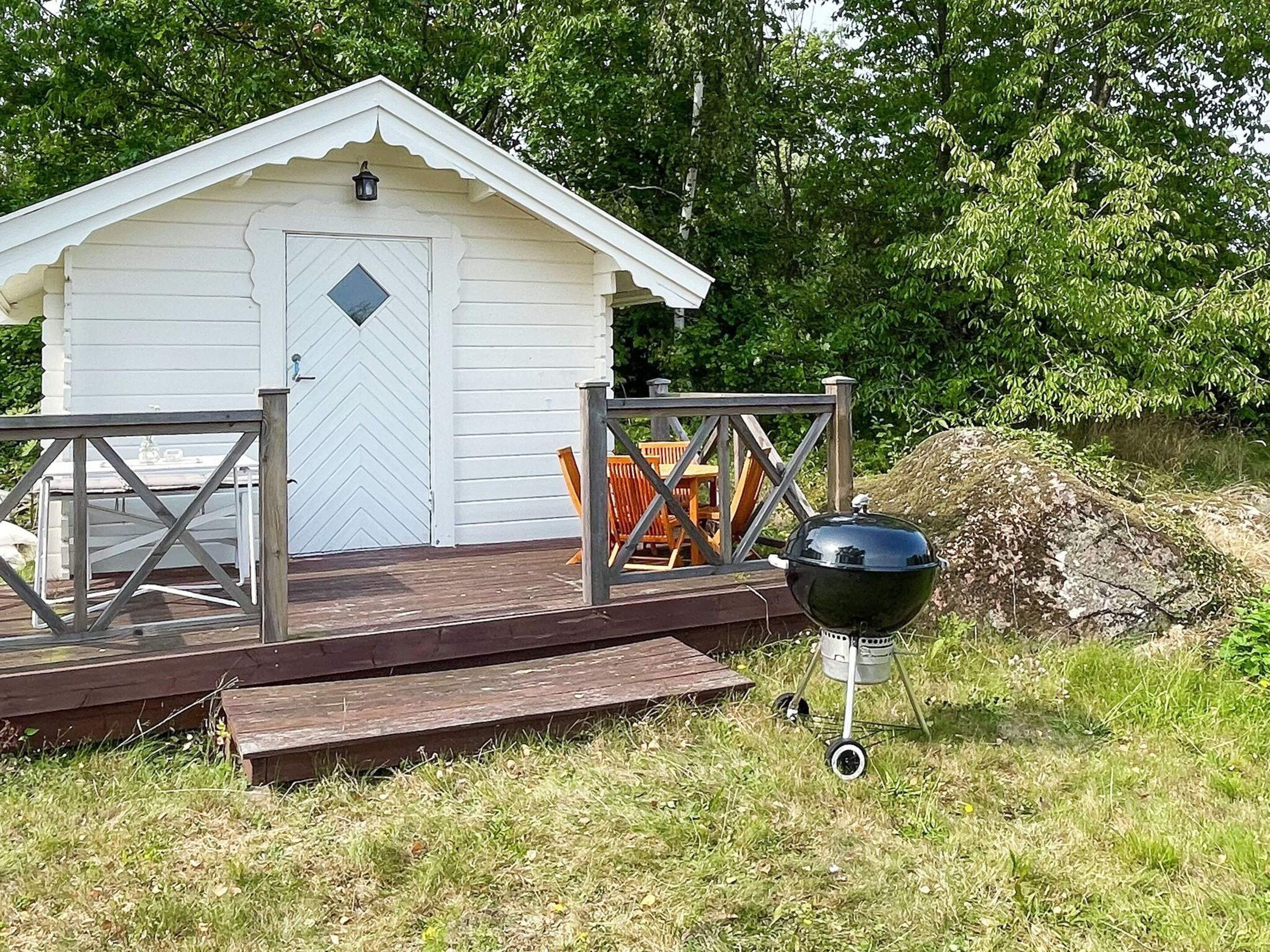 A small white cabin with a wooden deck, a grill, and outdoor furniture.