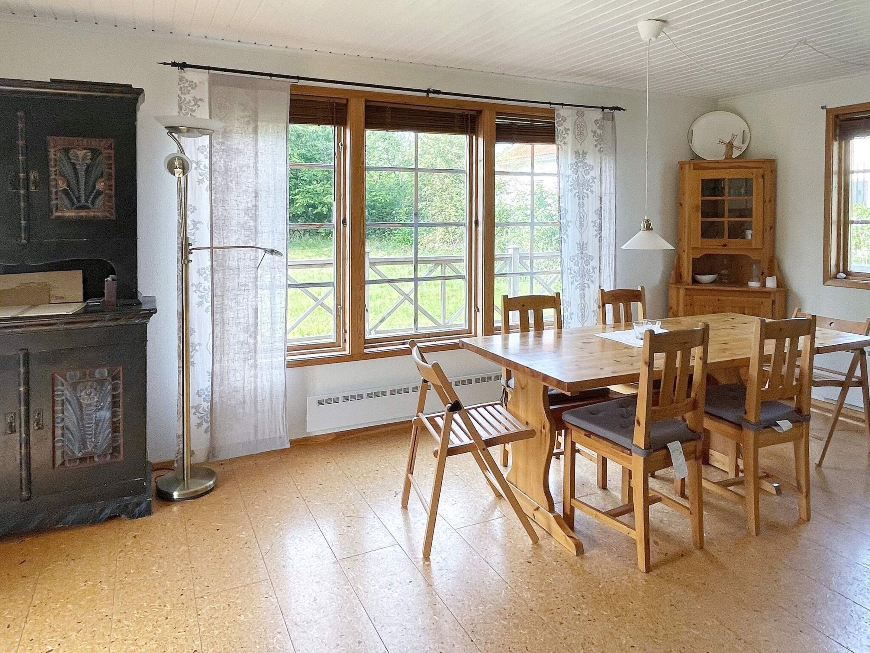 Un coin repas avec une table et des chaises en bois, un meuble avec des portes en verre et une fenêtre donnant sur un paysage verdoyant.