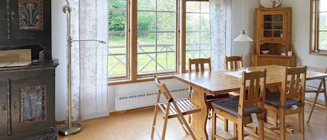 A dining area with a wooden table and chairs, a cabinet with glass doors, and a window with a view of greenery.