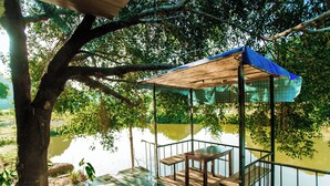 Een houten terras met een tafel en bankje, met uitzicht op kalm water, omringd door bomen.