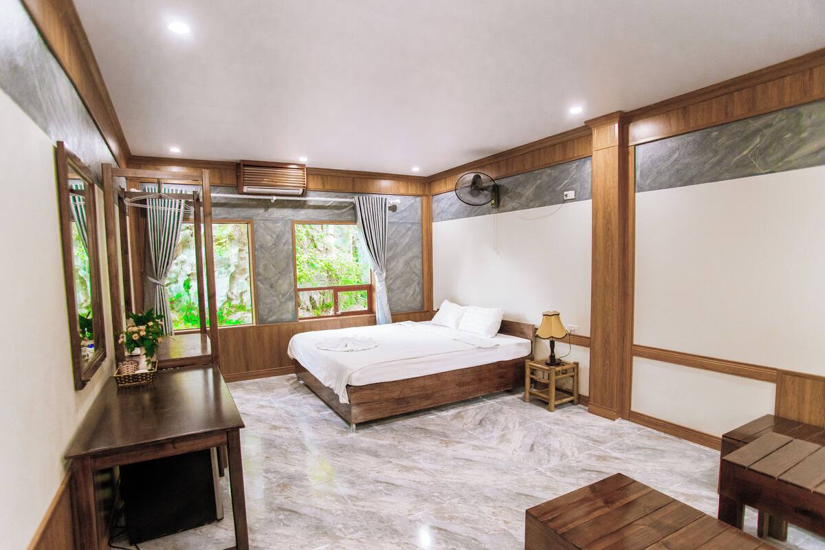 Een slaapkamer met een houten bed, een nachtkastje, een bijzettafeltje en een raam met gordijnen.