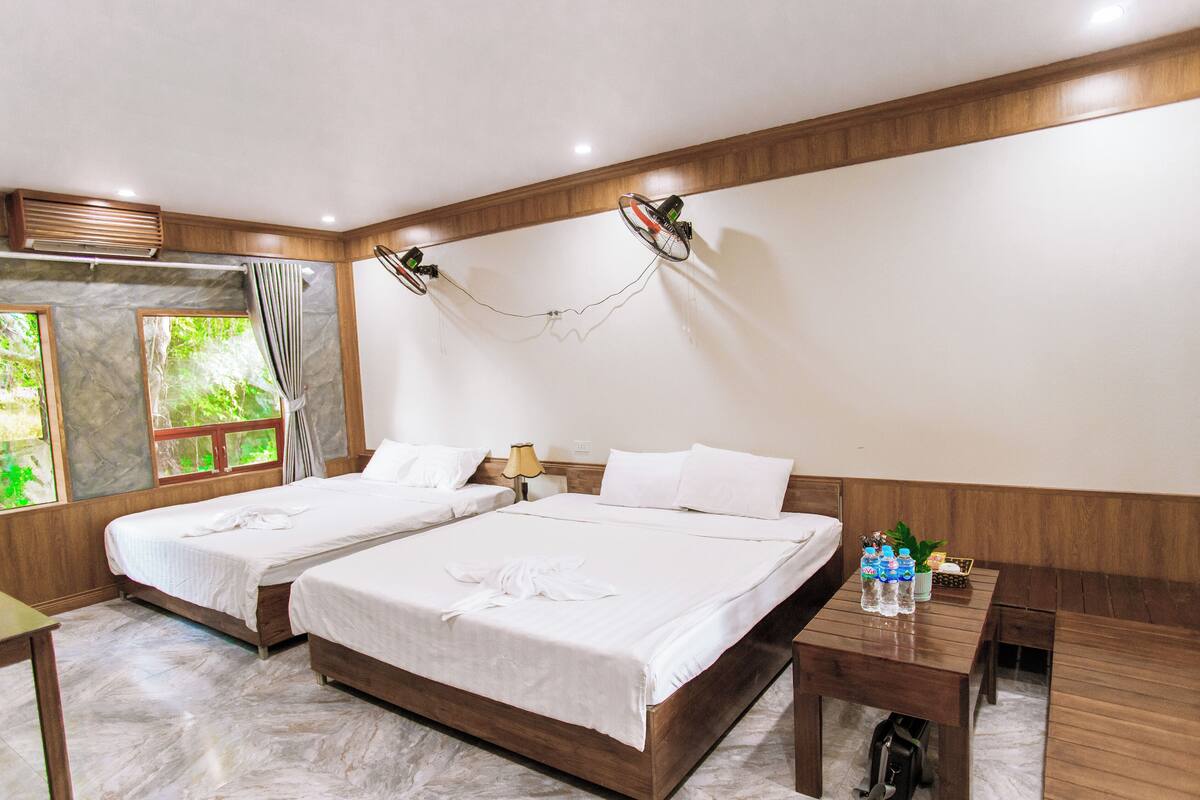 Een hotelkamer met twee bedden, een houten hoofdeinde, een nachtkastje, een lamp en een raam met gordijnen.