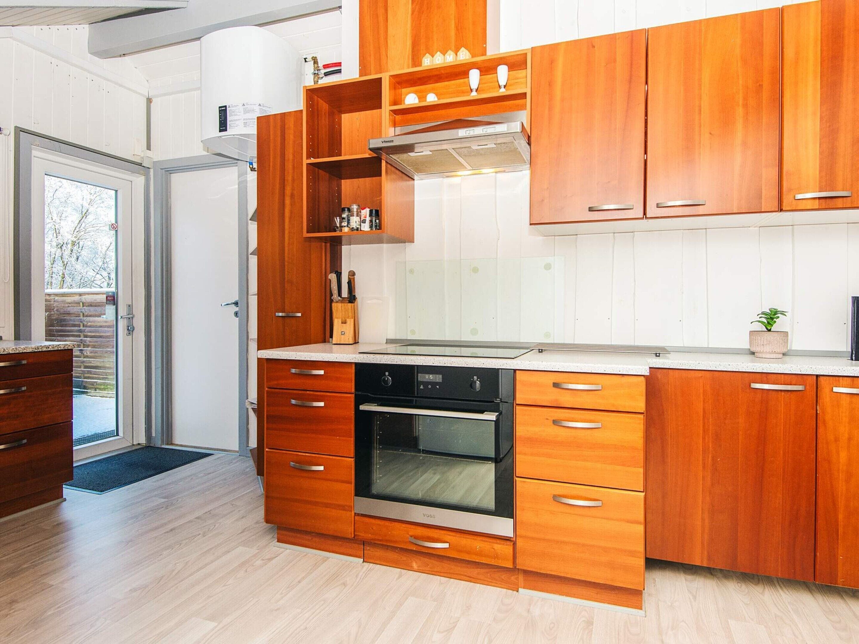 Une cuisine moderne avec des meubles en bois, un four encastré et une hotte de cuisine en acier inoxydable.