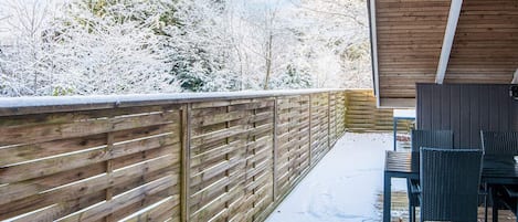 Eine Holzterrasse mit Metallgeländer, einem Tisch mit Stühlen und Blick auf schneebedeckte Bäume.