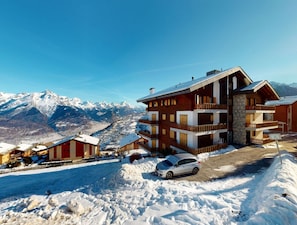 Un hotel de varios pisos con balcones, con una imponente montaña nevada al fondo.