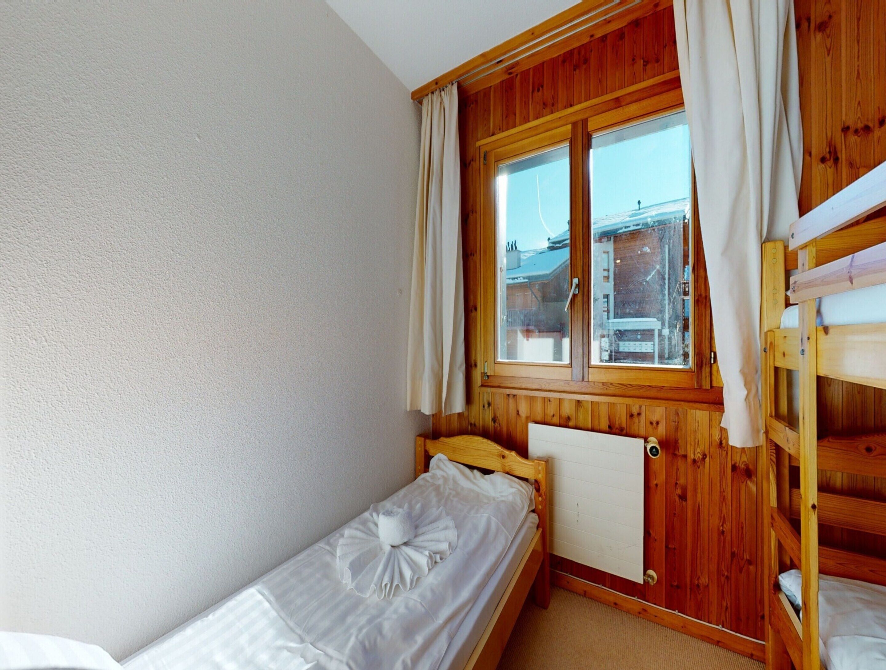 Una habitación pequeña y acogedora con una cama individual, una ventana con cortinas y una litera en la esquina.