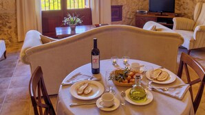 A dining area with a stone wall, a table set for two with plates, glasses, and a bottle of wine. - Agroturismo Roqueta (Maria de la Salut)
