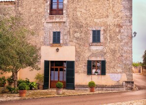 A stone building with a wooden door and shutters, potted plants, and a cobblestone street. - Agroturismo Roqueta (Maria de la Salut)