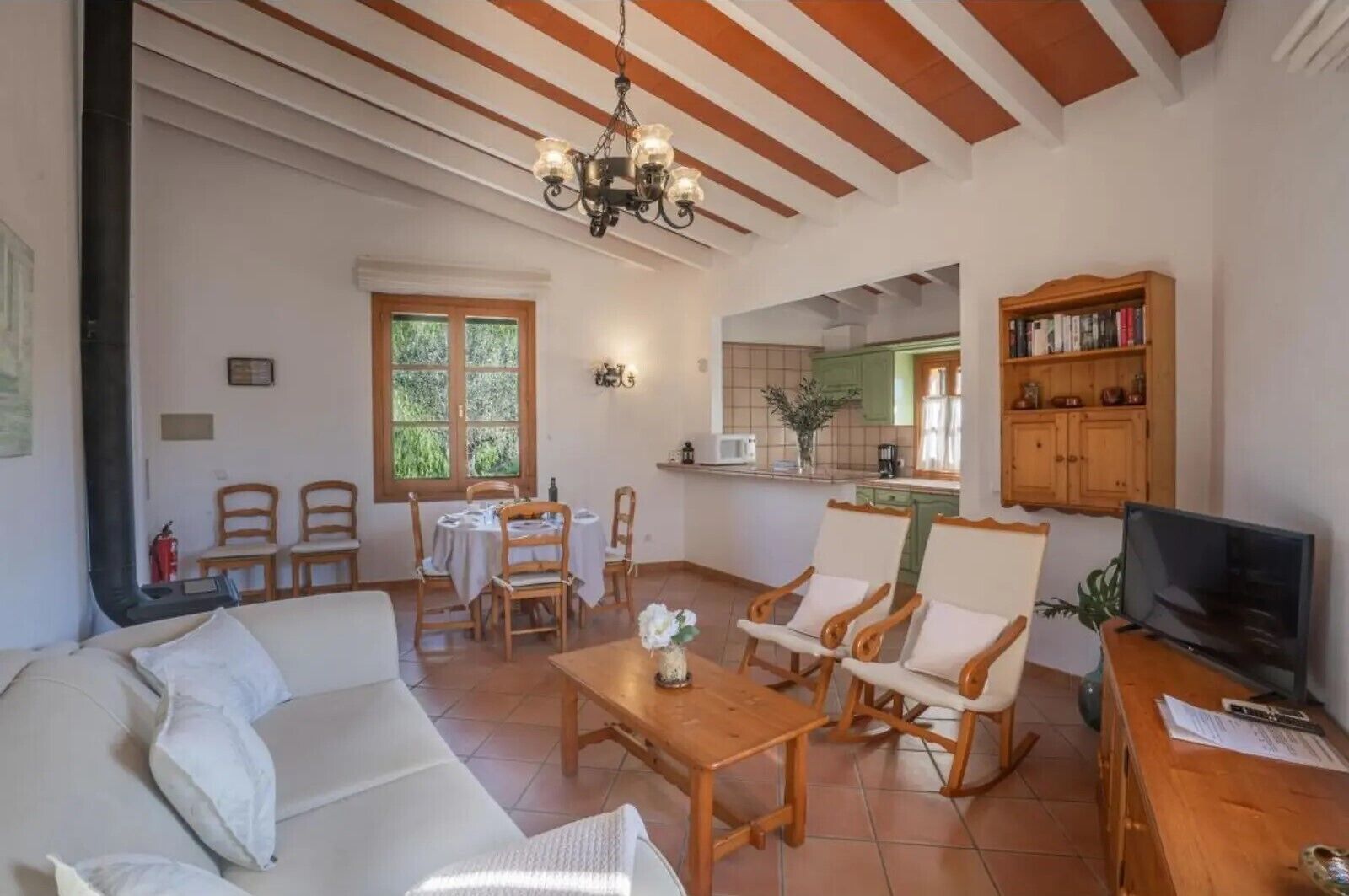 A living room with a sofa, chairs, a table, a TV, and a kitchen area in the background.
