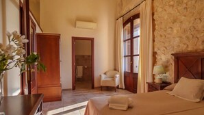 A hotel room with a bed, a chair, a nightstand with a lamp, and a wooden wardrobe. - Agroturismo Roqueta (Maria de la Salut)