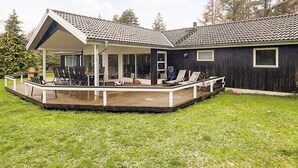 Ein Haus mit überdachter Terrasse, einer Holzterrasse und einem umzäunten Garten.