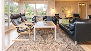 Ein gemütliches Wohnzimmer mit großem Fenster, einer schwarzen Ledersofa, einem schwarzen Ledersessel, einem weißen Couchtisch und einem gemusterten Teppich.