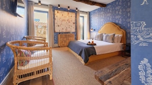 A bedroom with a large bed, a wooden headboard, a wicker chair, and a wooden bench. - THE PINTA Boutique Hotel (Armamar)