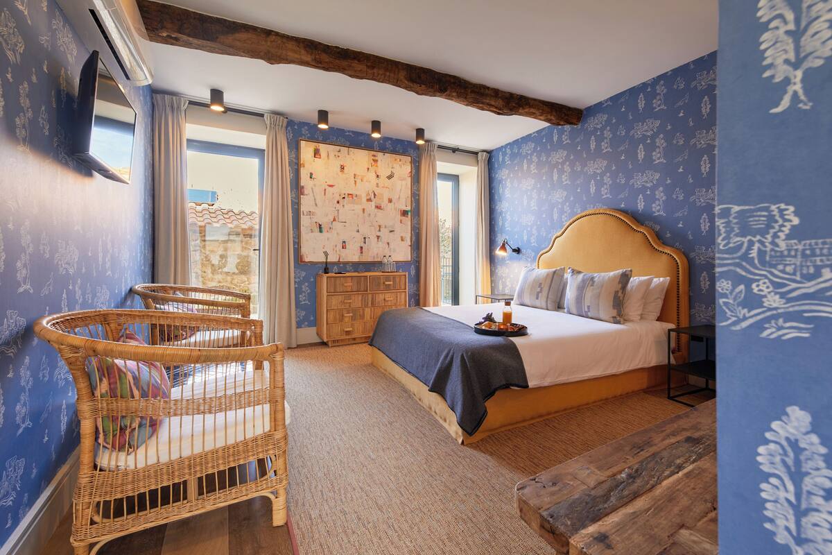 Ein Schlafzimmer mit einem großen Bett, einem Holzkopfstück, einem Korbstuhl und einer Holzbank.