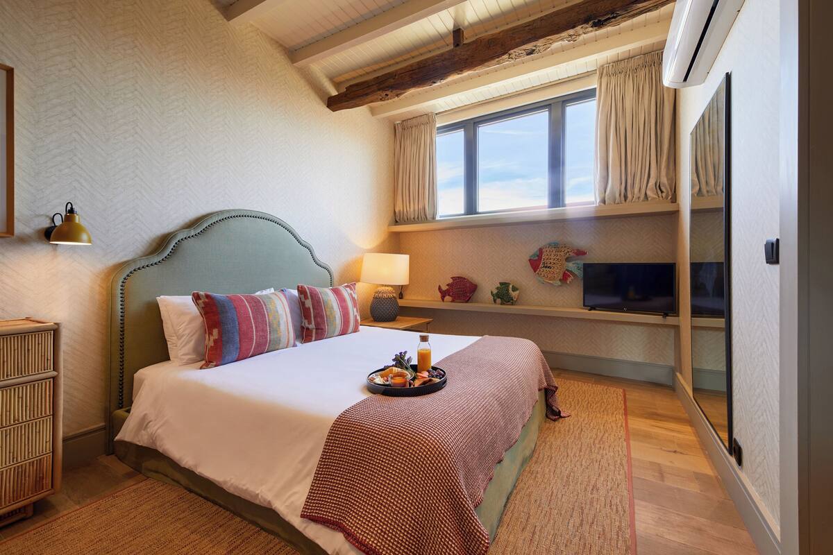 Ein Schlafzimmer mit einem Bett, einem Nachttisch, einem Fernseher und einem Fenster mit Vorhängen.