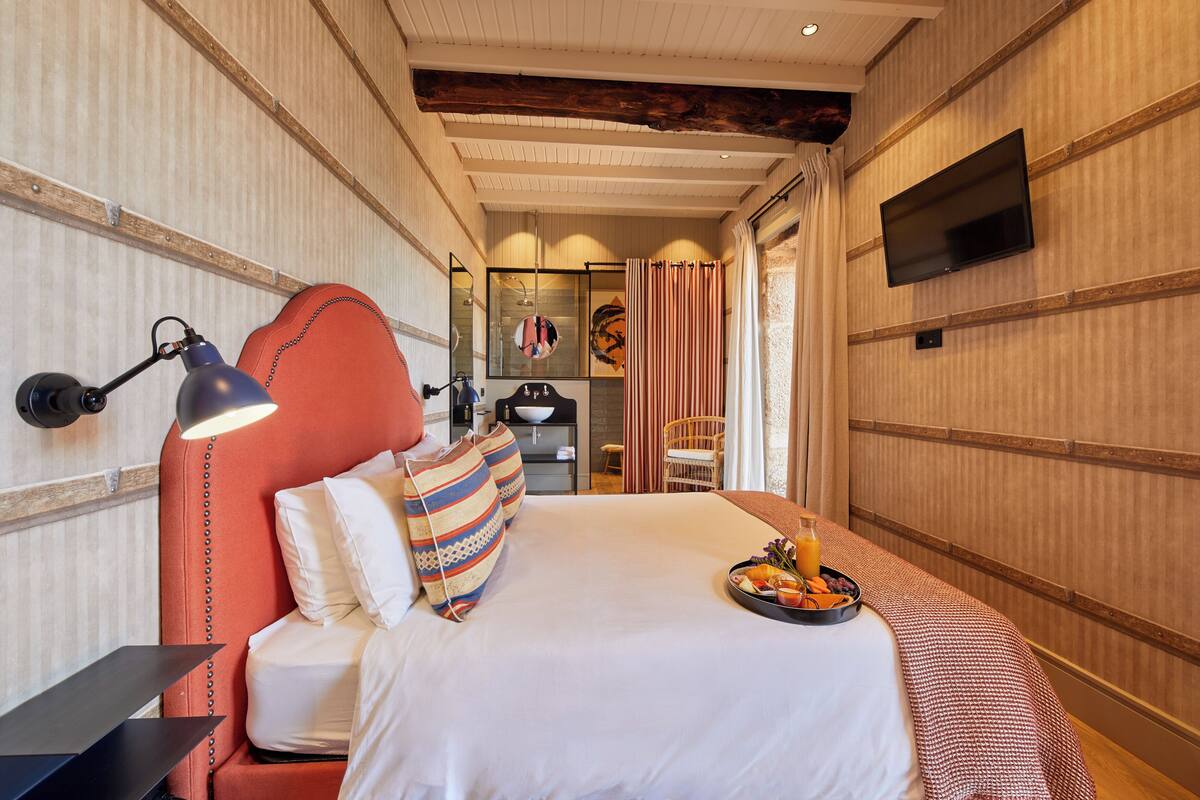 Ein Hotelzimmer mit Bett, Nachttisch, an der Wand montiertem Fernseher und Frühstückswagen auf dem Bett.