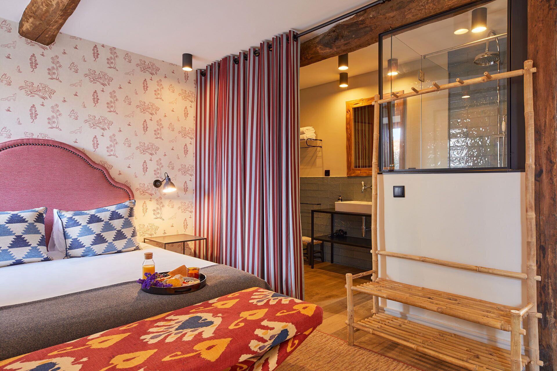 A bedroom with a bed, a bedside table with a lamp, a breakfast tray, and a window with a view of the bathroom.
