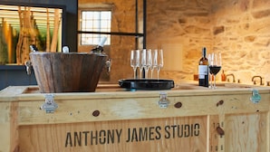 A wooden bar counter with a rustic design, labeled "ANTHONY JAMES STUDIO," featuring a large copper bucket, a black tray, and several wine glasses. - THE PINTA Boutique Hotel (Armamar)