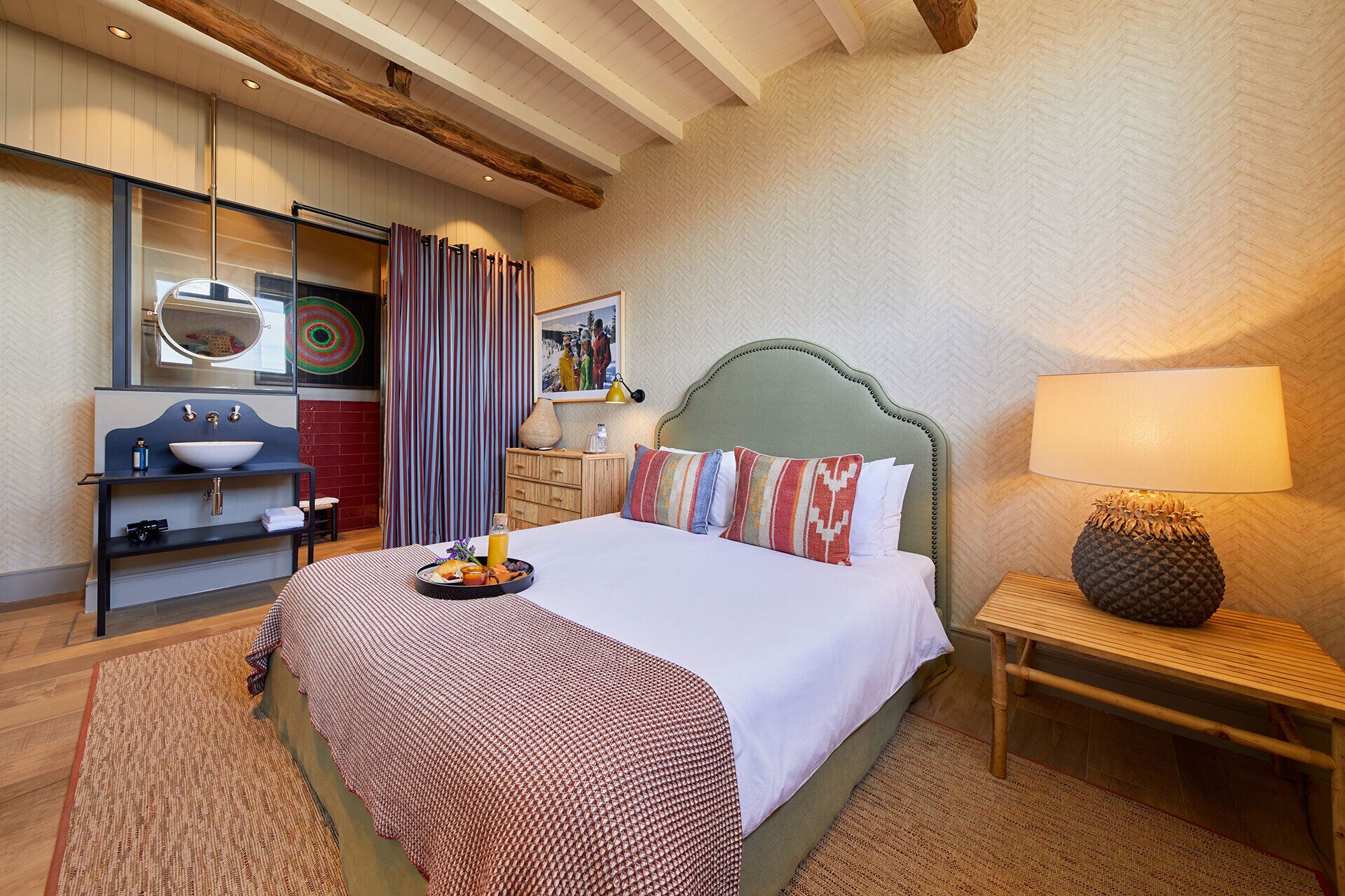 A hotel room with a bed, bedside table, lamp, and a bathroom with a sink and mirror.