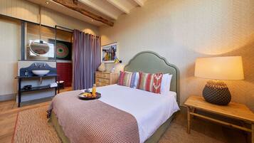 A hotel room with a bed, bedside table, lamp, and a bathroom with a sink and mirror.