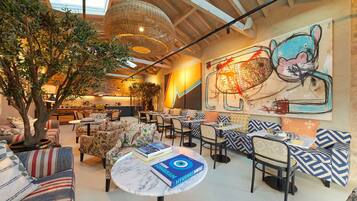 A cozy indoor dining area with round tables, cushioned seating, and a large wall mural.