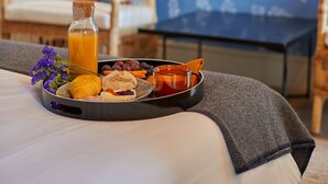 A breakfast tray with croissants, fruits, and juice on a bed in a room with a blue patterned wall and a television mounted on the wall. - THE PINTA Boutique Hotel (Armamar)