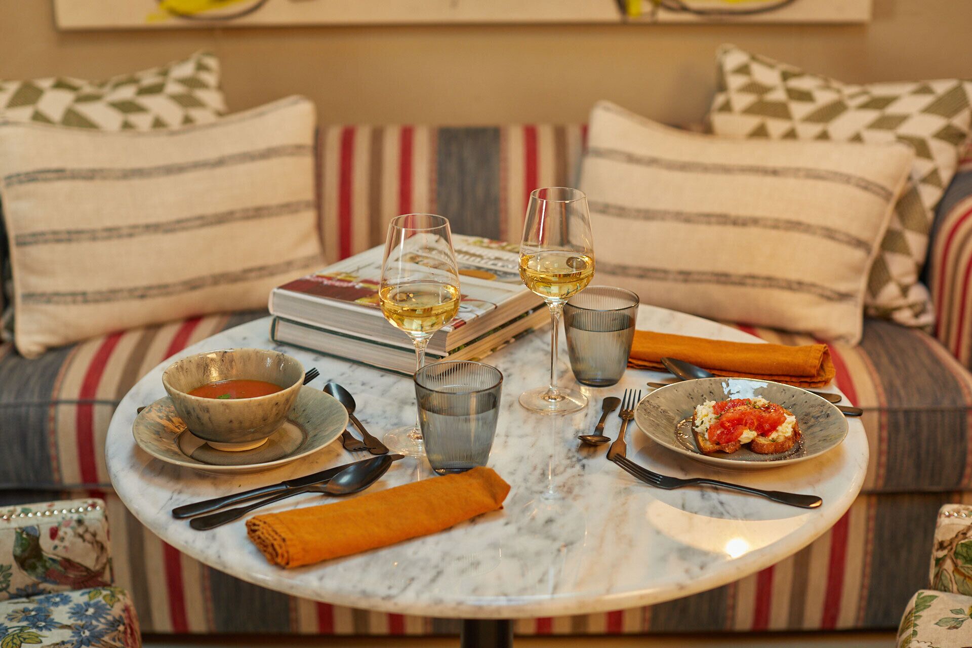 Uma mesa de mármore com taças de vinho, recipientes com comida e um livro.