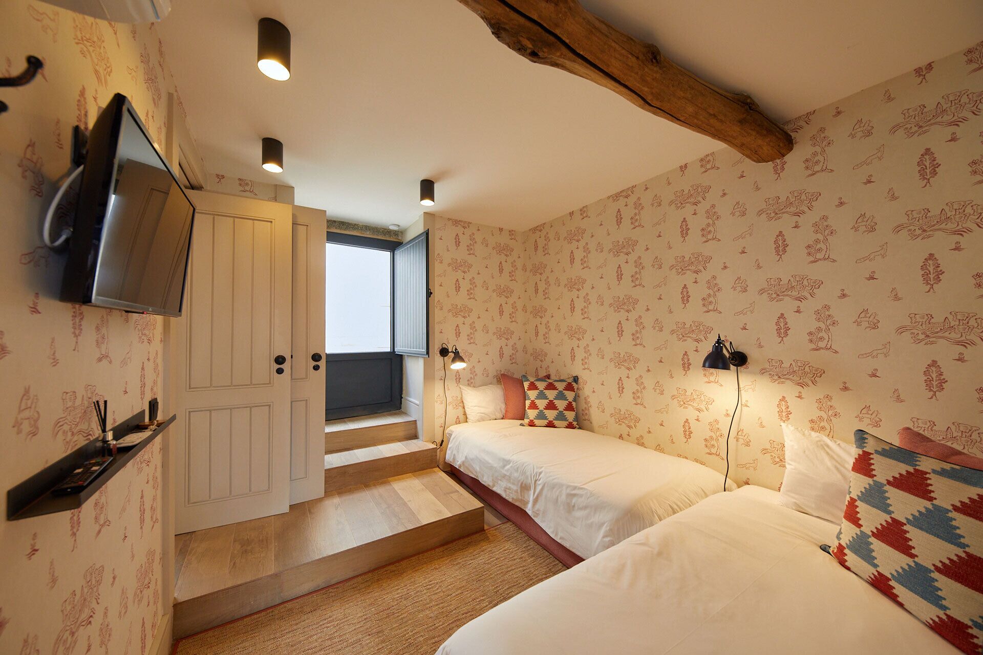 A bedroom with two beds, a TV, and a staircase leading to a balcony.